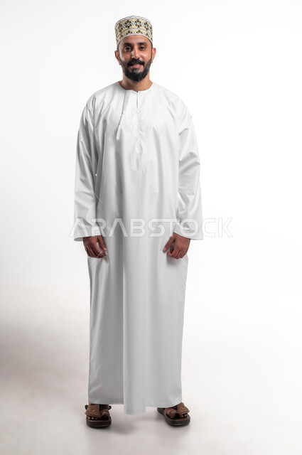 The concept of masculinity and self-confidence, taking personal photos for official documents, a portrait of a smiling Arab Gulf Omani young man wearing a dishdasha and a cuff, looking at the camera with gestures of pleasure and happiness, attention to elegance and external appearance, full-length body photo, white background