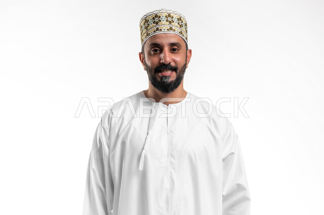 مفهوم الرجولة والثقة بالنفس، التقاط الصور الشخصية للوثائق الرسمية، بورتريه مقرب لشاب عربي خليجي عماني مبتسم يرتدي الدشداشة و الكمه ينظر الى الكاميرا بإيماءات السرور والسعادة، الاهتمام بالأناقة والمظهر الخارجي، خلفية بيضاء