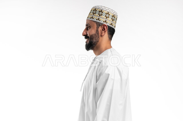 Concern with elegance and external appearance, the concept of masculinity and self-confidence, taking personal photos for official documents, a close-up portrait from the side of a smiling Arab Gulf Omani young man wearing a dishdasha and a cuff with gestures of pleasure and happiness, a white background