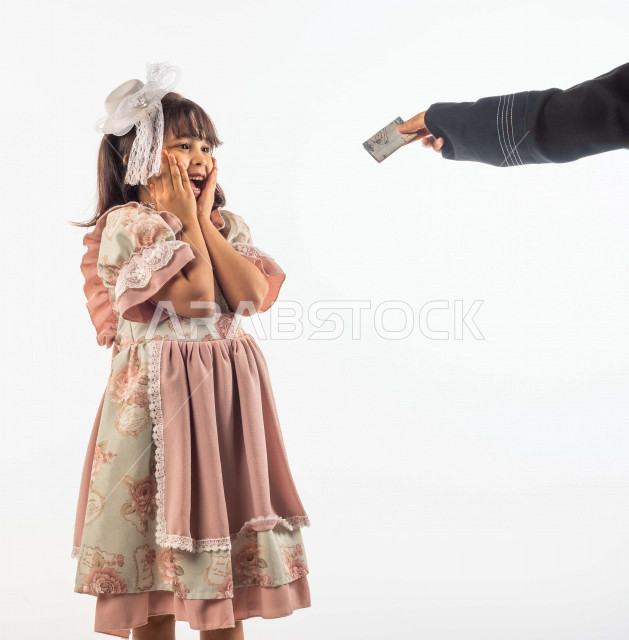 خلفية بيضاء لفتاه صغيرة سعودية خليجية مبتسمة وجميلة ، تضع يدها على خدها تدل على السعادة بالعيدية بإيماءات وجه ويدين مختلفة , بورتريه لطفلة سعودية خليجية سعيدة ترتدي لباس العيد الانيق ,الاحتفال بعيد الفطر السعيد, عيد الفطر المبارك , تقديم العيدية للأطفال