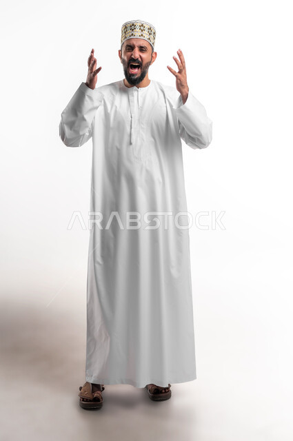 مفهوم الغضب و الإثاره والرغبة بالانتقام, بورتريه لشاب عربي خليجي عماني مبتسم يرتدي الدشداشة و الكمه يرفع يديه للاعلى بإيماءات الصراخ، الحزن والقهر من الخسارة، صورة الجسم بالطول الكامل، خلفية بيضاء