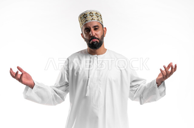 التردد وعدم الثقة بخصوص أمر معين، بورتريه مقرب لشاب عربي خليجي عماني يرتدي الدشداشة و الكمه  يرفع كفيه للاعلى بإيماءات عدم التأكد،  الشعور بالحيرة وعدم المعرفة، خلفية بيضاء
