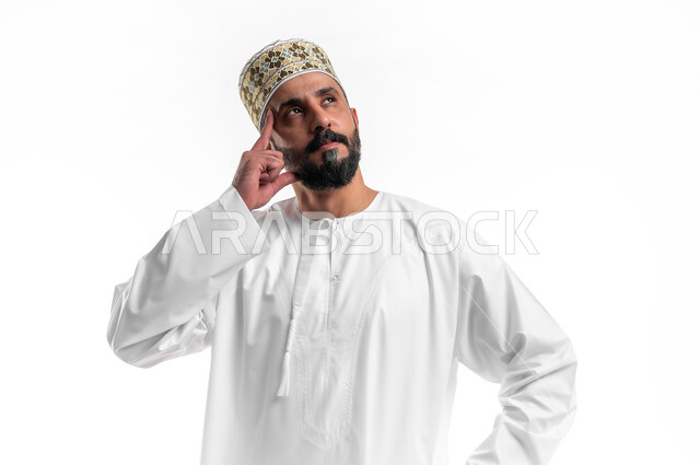 التركيز والتمعن لإيجاد الحل لمشكلة ما, حل المشكلات واتخاذ القرارات، بورتريه مقرب لشاب عربي خليجي عماني يرتدي الدشداشة و الكمه يضع يده على وجهه بإيماءات التفكير والحيرة، مفهوم التأمل بالمستقبل، خلفية بيضاء