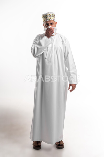 المرض والرشح والكحه والانفلونزا, الإحساس بالكسل والخمول، بورتريه لشاب عربي خليجي عماني يرتدي الدشداشة و الكمه يمسك بيده منديل، الاصابة بفايروس كورونا المستجد، صورة الجسم بالطول الكامل، خلفية بيضاء