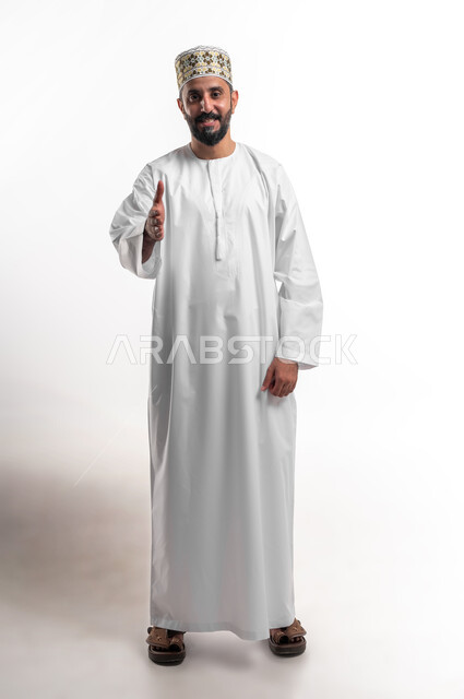 إلقاء التحيه والسلام, مفهوم الاستقبال والترحيب, التعارف و الصداقه وتكوين علاقات, بورتريه لشاب عربي خليجي عماني مبتسم يرتدي الدشداشة و الكمه ينظر الى الكاميرا يقوم بمد كفه للمصافحة بإيماءات السرور والبشاشة، خلفية بيضاء