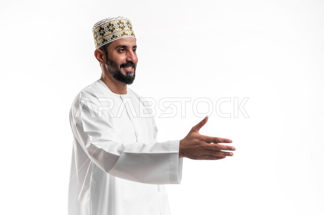 إلقاء التحيه والسلام, مفهوم الاستقبال والترحيب, التعارف و الصداقه وتكوين علاقات, بورتريه مقرب لشاب عربي خليجي عماني مبتسم يرتدي الدشداشة و الكمه يقوم بمد كفه للمصافحة بإيماءات السرور والبشاشة، خلفية بيضاء