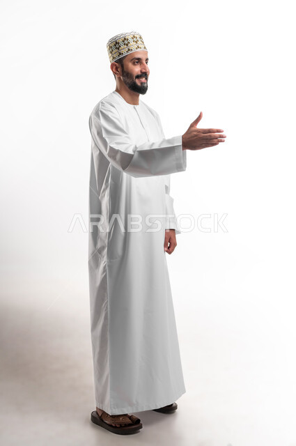 إلقاء التحيه والسلام, مفهوم الاستقبال والترحيب, التعارف و الصداقه وتكوين علاقات, بورتريه لشاب عربي خليجي عماني مبتسم يرتدي الدشداشة و الكمه يقوم بمد كفه للمصافحة بإيماءات السرور والبشاشة، خلفية بيضاء