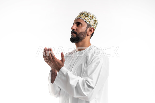 Diligence in worship and maintaining obedience, frequent supplication in the blessed month of Ramadan, close-up portrait of a young Arab Gulf Omani man wearing a dishdasha and a sleeve, raising his hands and calling upon God with gestures of supplication and supplication, white background