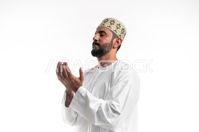 الإجتهاد في العبادة والحفاظ على الطاعات، الإكثار من الدعاء في شهر رمضان المبارك، بورتريه مقرب لشاب عربي خليجي عماني يرتدي الدشداشة و الكمه يرفع يديه ويدعو الله بإيماءات التوسل والتضرع، خلفية بيضاء