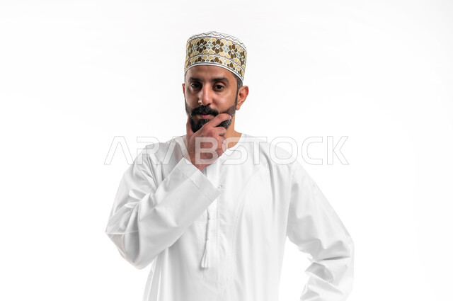 الشعور بالضيق والملل، التمعن والتركيز لإيجاد الحل لمشكلة ما, حل المشكلات واتخاذ القرارات، بورتريه مقرب لشاب عربي خليجي عماني يرتدي الدشداشة و الكمه يضع يده على وجهه بإيماءات التفكير والحيرة والانزعاج، خلفية بيضاء