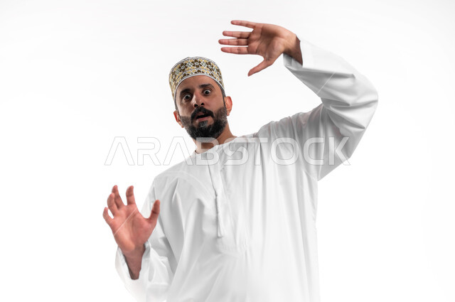 القلق والاحتياط والابتعاد عن شيء ما, حماية النفس من ضرر خارجي, بورتريه مقرب لشاب عربي خليجي عماني يرتدي الدشداشة و الكمه يرفع يديه للاعلى بإيماءات التوقف وعدم الاقتراب، مفهوم الحذر والصدمة، خلفية بيضاء