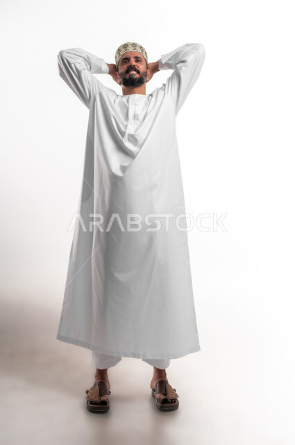 الشعور بالدهشة والصدمة والذهول, التفاجؤ من شيء ما، بورتريه لشاب عربي خليجي عماني مبتسم يرتدي الدشداشة و الكمه ينظر الى الكاميرا يضع يديه على رأسه بإيماءات التعجب والفرح, الشعور بالسعادة والقوة، خلفية بيضاء
