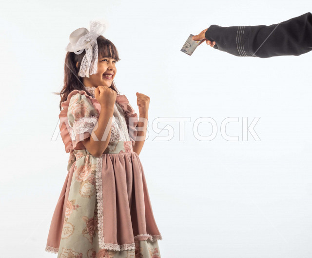 خلفية بيضاء لفتاه صغيرة سعودية خليجية مبتسمة وجميلة ، تنظر للعيدية بفرح بإيماءات وجه ويدين مختلفة , بورتريه لطفلة سعودية خليجية سعيدة ترتدي لباس العيد الانيق , الاحتفال بعيد الفطر السعيد ، عيد الفطر المبارك , تقديم العيدية للأطفال في عيد الفطر المبارك