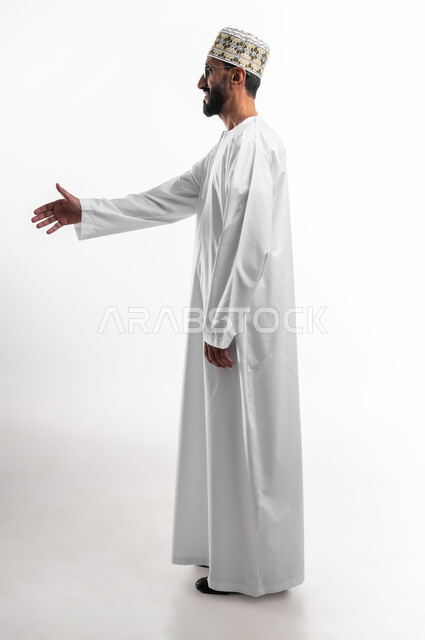 مد اليد للمصافحة وإلقاء التحية، بورتريه لرجل عربي عماني شايب يرتدي الدشداشة والكمه يقوم بمد كفه لرد السلام، ايماءات فرح وسرور، الاستقبال بوجه بشوش وسمح، حسن التعامل مع الآخرين، خلفية بيضاء