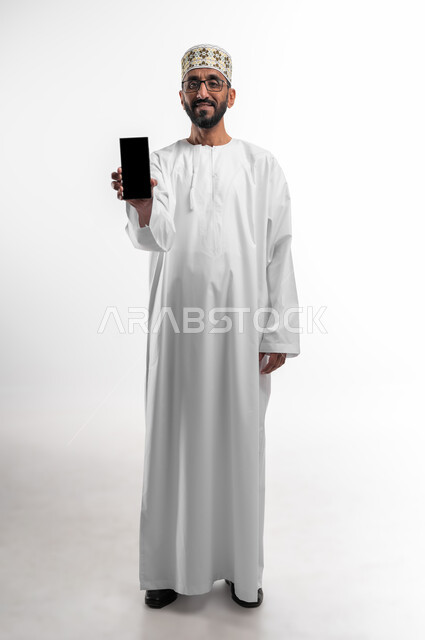The concept of technical and technological developments, a portrait of an old Omani Arab man wearing a dishdasha and a cuff, displaying a blank black screen on a mobile phone, keeping pace with modern progress, a white background.