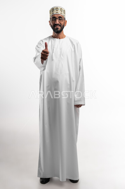 رفع إصبع الإبهام للأعلى دليل على الإعجاب، ايماءات تدل على الموافقة والقبول، بورتريه لرجل عربي عماني شايب يرتدي الدشداشة والكمه تظهر عليه تعابير الفرح والسرور ، الرضى وعدم الرفض، خلفية بيضاء