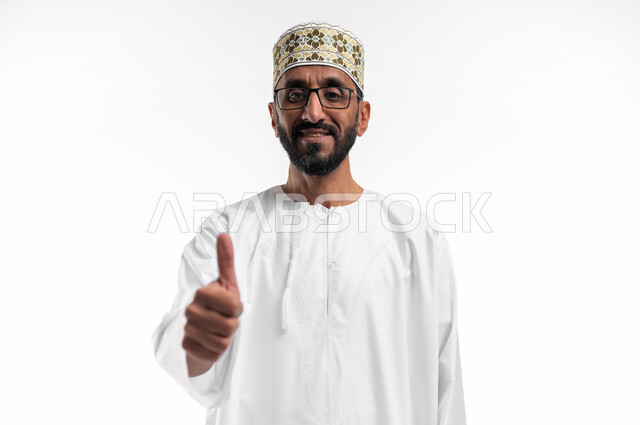 رفع إصبع الإبهام للأعلى دليل على الإعجاب، ايماءات تدل على الموافقة والقبول، بورتريه لرجل عربي عماني شايب يرتدي الدشداشة والكمه تظهر عليه تعابير الفرح والسرور ، الرضى وعدم الرفض، خلفية بيضاء