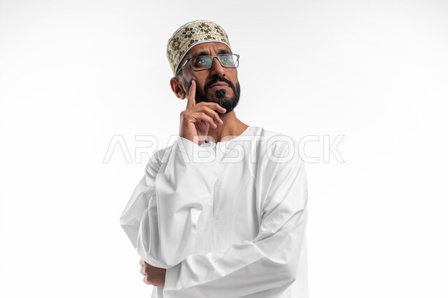 التفكير والتخطيط لشيء ما، ايماءات وجه تدل على التمعن والتدقيق، بورتريه لرجل عربي عماني شايب يرتدي الدشداشة والكمه ينظر للافق بعمق، مفهوم النظرة المستقبلية، خلفية بيضاء