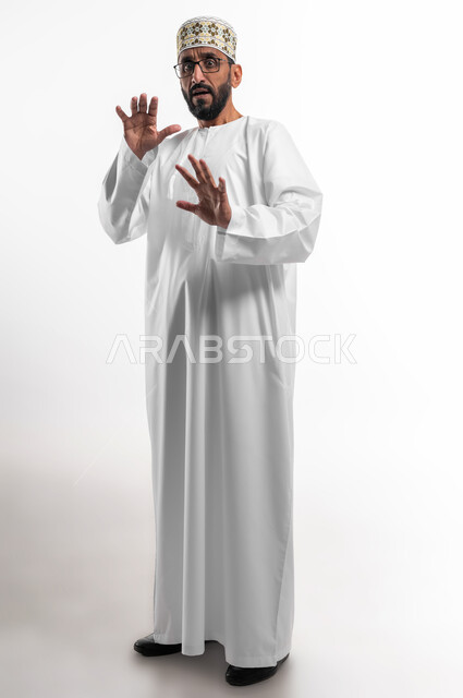 تعابير الذعر والخوف من شيء ما، مد اليدين للأمام محاولةً للدفاع عن النفس، بورتريه لرجل عربي عماني شايب يرتدي الدشداشة والكمه تظهر عليه علامات الرعب، ايماءات تدل على طلب النجدة والانقاذ، خلفية بيضاء