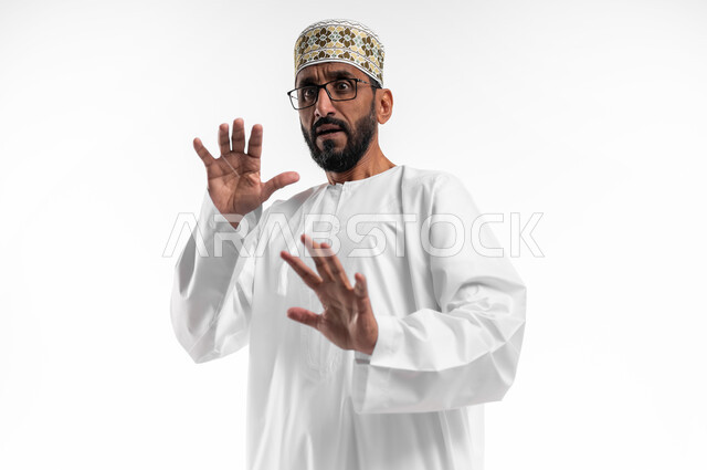 تعابير الذعر والخوف من شيء ما، مد اليدين للأمام محاولةً للدفاع عن النفس، بورتريه لرجل عربي عماني شايب يرتدي الدشداشة والكمه تظهر عليه علامات الرعب، ايماءات تدل على طلب النجدة والانقاذ، خلفية بيضاء