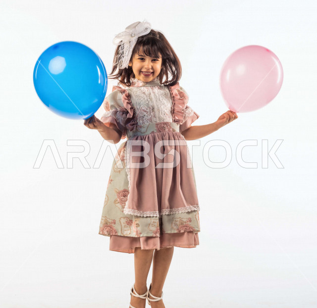 خلفية بيضاء لفتاه صغيرة سعودية خليجية مبتسمة وجميلة ، تنظر الى الكاميرا وتحمل بيدها الأولى بالون أزرق وبيدها الأخرى زهري بإيماءات وجه ويدين مختلفة , بورتريه لطفلة سعودية خليجية سعيدة ترتدي لباس العيد الانيق, الاحتفال بعيد الفطر السعيد ،عيد الفطر المبارك