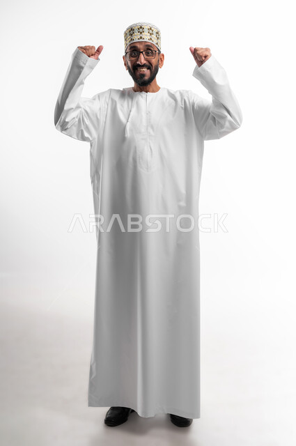 ايماءات وجه تدل على الحماس الزائد، بورتريه لرجل عربي عماني شايب يرتدي الدشداشة والكمه يرفع يده للأعلى للتشجيع، تعابير فرح وسرور، الافتخار والشعور بالسعادة لإنجاز شيء ما، خلفية بيضاء