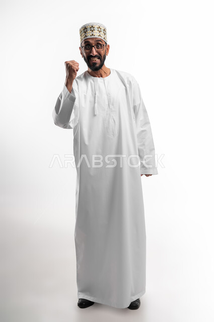 ايماءات وجه تدل على الحماس الزائد، بورتريه لرجل عربي عماني شايب يرتدي الدشداشة والكمه يرفع يده للأعلى للتشجيع، تعابير فرح وسرور، الافتخار والشعور بالسعادة لإنجاز شيء ما، خلفية بيضاء