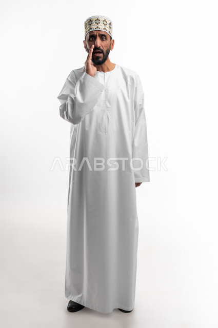 ايماءات خوف وتحذير، بورتريه لرجل عربي عماني شايب يرتدي الدشداشة والكمه يقوم بمناداة شخص ما بالخفية، تعابير وجه تدل على التنبيه من حدوث مصيبة ما، خلفية بيضاء