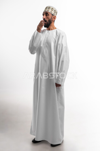 التثاؤب والرغبة في النوم، وضع اليد على الفم دليل على الشعور بالنعاس، بورتريه لرجل عماني شايب يرتدي الدشداشة والكمه تظهر عليه علامات النعس، تعابير وجه تدل على التعب وعدم المقاومة، خلفية بيضاء