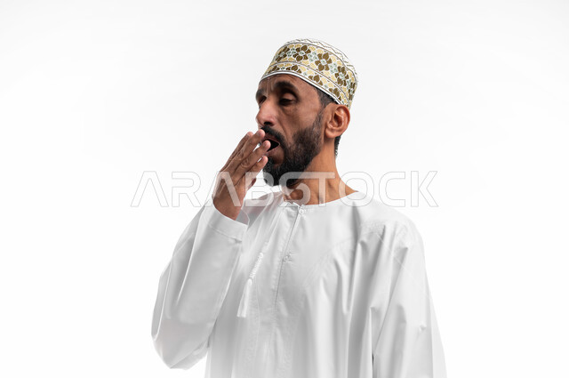 التثاؤب والرغبة في النوم، وضع اليد على الفم دليل على الشعور بالنعاس، بورتريه لرجل عماني شايب يرتدي الدشداشة والكمه تظهر عليه علامات النعس، تعابير وجه تدل على التعب وعدم المقاومة، خلفية بيضاء