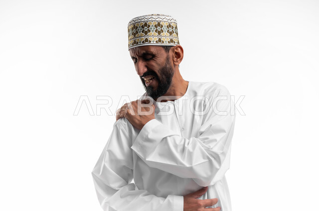 Feeling severe pain that is difficult to bear in the shoulder, difficulty moving and folding the arm, a portrait of an old Omani man wearing a dishdasha and a cuff suffering from pain in his joints, facial gestures indicating pain, a white background.
