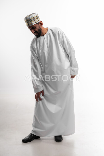 الإحساس بألم في الركبة والمفاصل، الانزعاج والصعوبة بالمشي، آلام شديدة صعبة التحمل، بورتريه لرجل عماني شايب يرتدي الدشداشة والكمه تظهر عليه علامات التعب، خلفية بيضاء