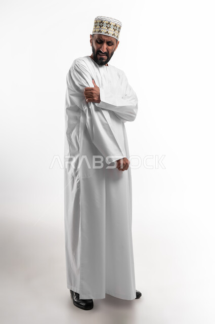 الوجع العضلي نتيجة الآلام العصبية، طلب المساعده والحاجه للعلاج، التهاب العضلات والمفاصل، بورتريه لرجل عربي خليجي عماني كبير بالسن يرتدي الدشداشة و الكمه يضع يده على مكان الوجع بايماءات الألم والتعب والارهاق، حالة اسعافية طارئة, الجسم بالطول الكامل, خلفية بيضاء