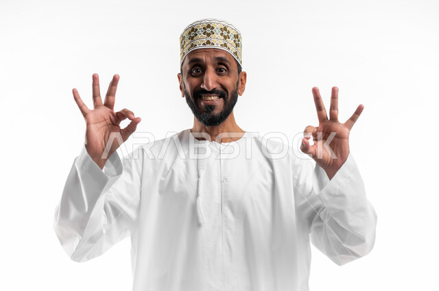تعابير عن التميز والامتياز بإشارة لحالة ممتازة, بورتريه مقرب لرجل كبير السن عربي خليجي عماني يرتدي الدشداشة والكمه  بإيماءات  القبول والامتياز, علامة الجودة والإتقان,  خلفية بيضاء.