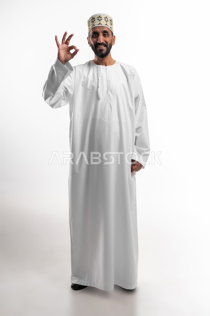 التعبير عن الجودة والإتقان, بورتريه لرجل كبير السن عربي خليجي عماني يرتدي الدشداشة والكمه  يرفع يده للأعلى  بإيماءات   الرضا والقبول والأعجاب, النظر الى الكاميرا بتعابير السرور, صورة الجسم بالطول الكامل, خلفية بيضاء.