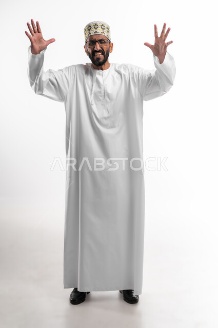 مفهوم الغضب والانفعال, بورتريه لرجل كبير السن  عربي خليجي عماني يرتدي الدشداشة والكمه و النظارات الطبية يرفع يديه عاليا  بإيماءات التوتر , تعابير الصراخ والضغط النفسي, صورة الجسم بالطول الكامل, خلفية بيضاء.