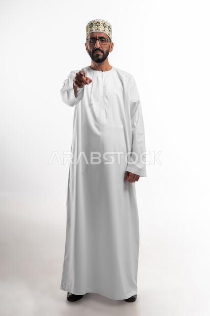 الشعور بالانزعاج وطلب التوقف عن فعل الأخطاء, بورتريه  لرجل كبير السن عربي خليجي عماني يرتدي الدشداشة والكمه والنظارات الطبية يرفع اصبع السبابة للأعلى  بإيماءات الغضب والعبوس,  تعابير  الاتهام والتوبيخ  وإلقاء اللوم, التوبيخ والاتهام,  صورة الجسم بالطول الكامل, خلفية بيضاء.