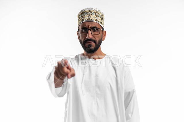 الشعور بالانزعاج وطلب التوقف عن فعل الأخطاء, بورتريه مقرب لرجل كبير السن عربي خليجي عماني يرتدي الدشداشة والكمه والنظارات الطبية يرفع اصبع السبابة للأعلى  بإيماءات الغضب والعبوس,  تعابير  الاتهام والتوبيخ  وإلقاء اللوم, التوبيخ والاتهام, خلفية بيضاء.