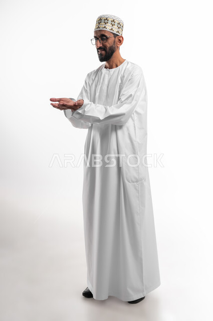A hand movement indicating a request for help and assistance, extending the palms forward to indicate need, a portrait of an old Omani man wearing a dishdasha, a cuff, and medical glasses, the traditional dress for men in the Sultanate of Oman, gestures of helplessness and hope, white background.