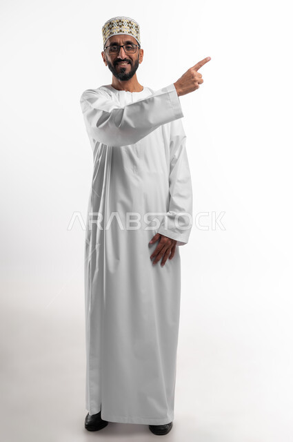 مد اليد إشارةً لشيءٍ ما بواسطة إصبع السبابة، شد الإنتباه ولفت النظر، ايماءات سعادة وفرح، بورتريه لرجل عماني شايب يرتدي الدشداشة والكمه ونظارات طبيه، الجسم بالطول الكامل، الزي التقليدي للرجال في سلطنة عمان، خلفيه بيضاء