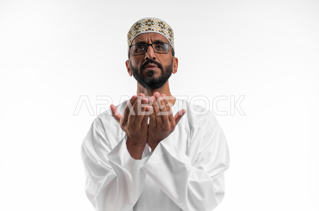 رفع اليدين للأعلى بهدف الدعاء والتضرع إلى الله تعالى،ايماءات التوسل والاسترحام، طلب المساعدة من المولى عز وجل، بورتريه لرجل عماني شايب يرتدي الدشداشة والكمه يدعي ويطلب المغفرة، خلفية بيضاء