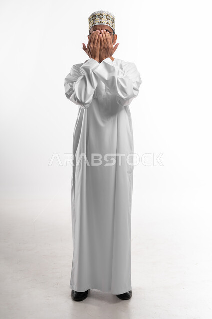 مسح الوجه باليدين دليل على الانتهاء من الدعاء، حركة اليد تدل على قول آمين، بورتريه لرجل عماني شايب يرتدي الدشداشة والكمه يدعي ويتوسل إلى الله، خلفية بيضاء