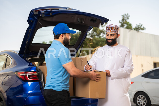 مفهوم التسوق الالكتروني, خدمات الشحن ذات الجودة العالية, عملية شراء المنتجات أونلاين, شاب عربي خليجي عماني يرتدي الدشداشة و الكمة يقوم بالتوقيع على أوراق و مستندات للتأكيد على استلام الطرد، مندوب يقوم بتوصيل طلبات الزبائن
