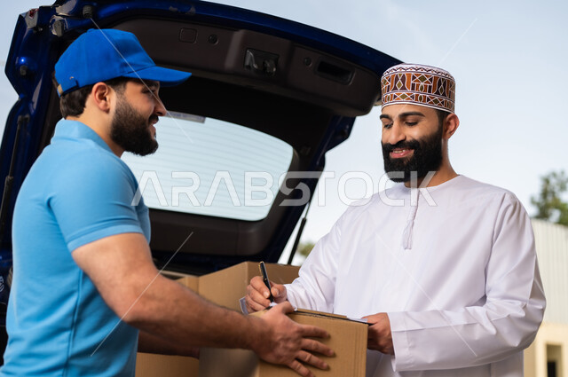 عمليات الشراء أونلاين, طلب المنتجات عبر الانترنت, مفهوم التسوق الالكتروني, خدمات الشحن ذات الجودة العالية, شاب عربي خليجي عماني يرتدي الدشداشة و الكمة يقوم بالتوقيع على أوراق و مستندات للتأكيد على استلام الطرد، مندوب يقوم بتوصيل طلبات الزبائن