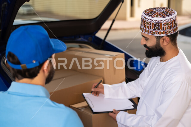 طلب المنتجات عبر الانترنت, مفهوم التسوق الالكتروني, خدمات الشحن ذات الجودة العالية, عمليات الشراء أونلاين, شاب عربي خليجي عماني يرتدي الدشداشة و الكمة يقوم بالتوقيع على أوراق و مستندات للتأكيد على استلام الطرد، مندوب يقوم بتوصيل طلبات الزبائن