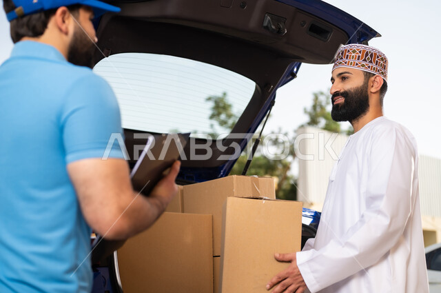 شحن الطلبات للزبائن، عملية التوصيل الآمنة والموثوقة ,مفهوم التسوق الالكتروني, شاب عربي خليجي عماني يرتدي الدشداشة و الكمة يقوم باستلام المشتريات، مندوب يحمل بيده أوراق و مستندات تأكيد تسليم الطرد للزبون
