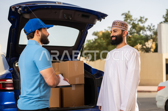Shipping orders to customers, the safe and reliable delivery process, the concept of electronic shopping, an Arab Gulf Omani young man wearing a dishdasha and a cuff receiving purchases, a representative holding in his hand papers and documents confirming the delivery of the package to the customer