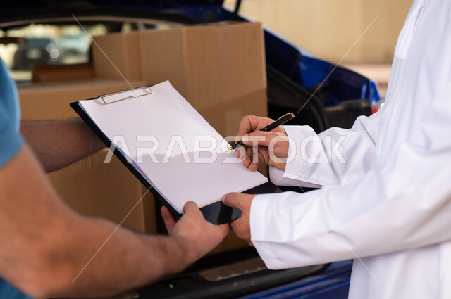 خدمات الشحن ذات الجودة العالية, عملية شراء المنتجات أونلاين, مفهوم التسوق الالكتروني, صورة مقربة ليد شاب عربي خليجي عماني يرتدي الدشداشة و الكمة يقوم بالتوقيع على أوراق و مستندات للتأكيد على استلام الطرد، مندوب يقوم بتوصيل طلبات الزبائن