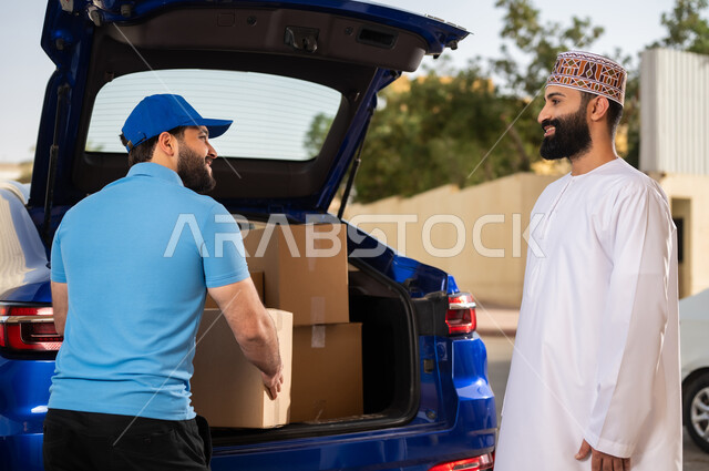 عملية الشحن السريع ذات الجودة العالية، طلب المنتجات عبر الإنترنت، مفهوم التسوق الالكتروني, شاب عربي خليجي عماني يرتدي الدشداشة و الكمة يستلم طرد المشتريات, مندوب يقوم بتسليم طلبات الزبائن