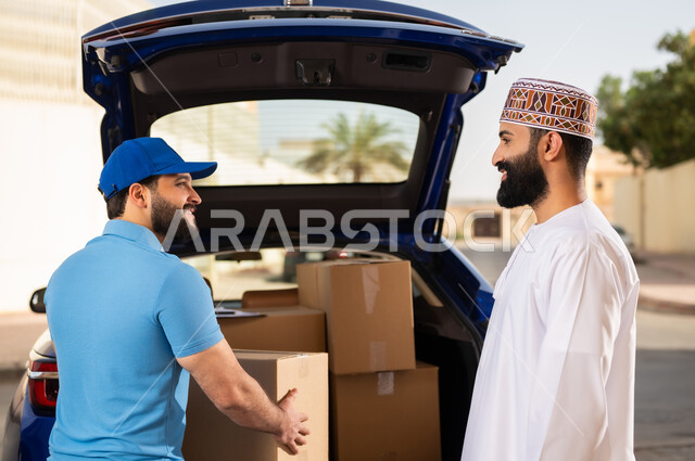 عملية الشحن السريع ذات الجودة العالية، طلب المنتجات عبر الإنترنت، مفهوم التسوق الالكتروني, شاب عربي خليجي عماني يرتدي الدشداشة و الكمة يستلم طرد المشتريات, مندوب يقوم بتسليم طلبات الزبائن